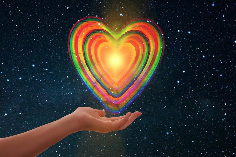 Mano sosteniendo un corazón de colores en la noche. Libros de salud espiritual y autoconocimiento.